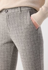 Grijs houndstooth-gepatroneerde broeken met een op maat gemaakte pasvorm, voorkruiszakken en een enkele zwarte knop op de tailleband. Gevoelige stofdetails zichtbaar.