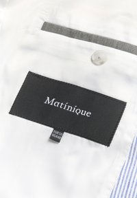 Mustad musta ristkülikukujuline riideetikett, millel on valge kangast "Matinique" õmmeldud, suurusetikett EUR 50 US 40 ja selge nupp kohal.