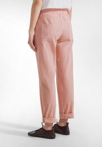 Różowe spodnie o krótkim kroju i luźnym fasonie, z elastycznym pasem, bocznymi kieszeniami oraz obszytymi końcami; zestawione z ciemnobrązowymi sznurowanymi butami.