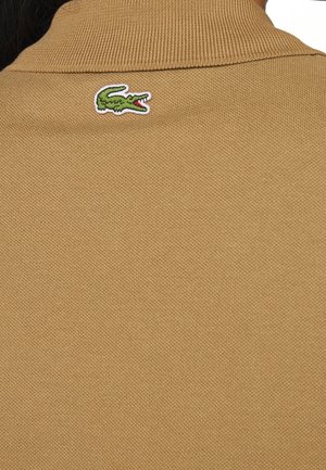 Braunes Poloshirt mit geripptem Kragen, das auf der Rückseite ein gesticktes grünes Krokodil-Logo aufweist, aus strukturiertem Baumwollstoff gefertigt.