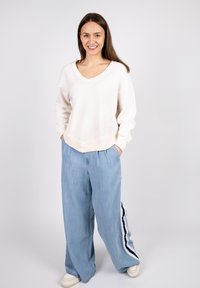 Light beige V-neck sweatshirt with long sleeves and stitched details, paired with loose, light blue wide-leg trousers featuring side stripes.