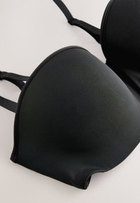Sutien negru căptușit cu bretele reglabile așezat plat pe o suprafață deschisă, arătând material neted și forme curbate ale cupelor.