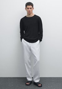 Schwarzes, geripptes Langarmshirt, weiße Leinenhosen und schwarze Sandalen. Das Outfit hat eine lockere Passform und ein minimalistisches Design.