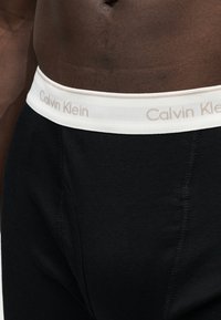 Ανδρικός κορμός που φορά μαύρα εσώρουχα Calvin Klein με λευκή μέση με το όνομα της μάρκας.