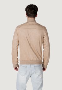 Giubbotto bomber in camoscio beige con polsini e orlo a coste, caratterizzato da un design minimalista e una texture morbida. Cuciture e dettagli della cucitura posteriore visibili.