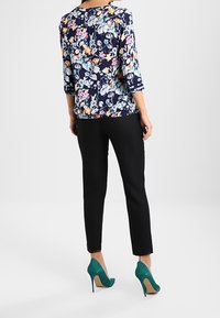 Top a fantasia floreale blu navy con maniche a tre quarti, abbinato a pantaloni neri slim. La modella indossa tacchi alti turchesi.