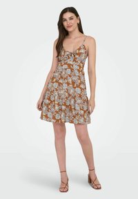 Bruine bloemenjurk met dunne bandjes, ruffles rond de halslijn en een uitlopende rok. Kenmerken zijn blauw en witte bloemenpatronen en een casual ontwerp.
