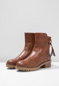 Bottines en cuir marron avec un bout arrondi, des panneaux latéraux et un talon épais. Présente des franges à l'arrière pour le détail.
