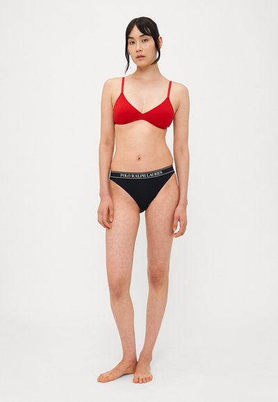 Sarkans trīsstūriska krūšturis ar plānām siksniņām, apvienots ar melniem bikini apakšbiksēm ar logotipa vidukļa joslu. Gluda tekstūra, minimālistisks dizains.