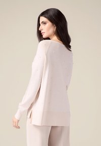Jersey de manga larga rosa claro con escote redondeado, que presenta adornos similares a perlas distribuidos de manera uniforme y acentos de canalé en el dobladillo y los puños.