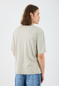 Hellgraues, übergroßes T-Shirt aus Baumwolle mit kurzen Ärmeln und Rundhalsausschnitt. Glatte Textur und lässiger Schnitt.