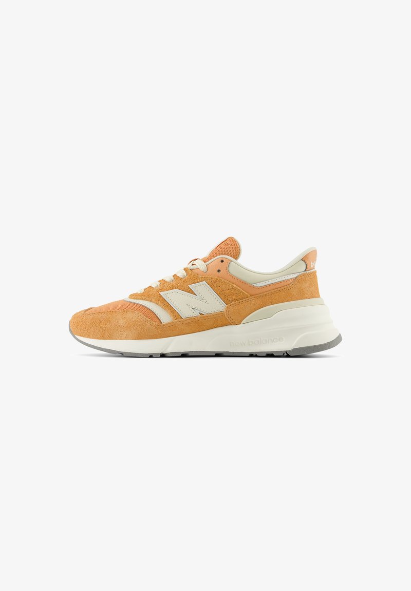 Sneaker New Balance orange et beige avec des panneaux en suède et en mesh, lacets blancs et une semelle blanche épaisse sur fond blanc.