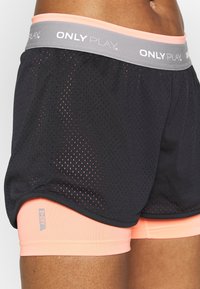 Shorts de sport en maille noire avec une ceinture grise et pêche. Présente une doublure intérieure pêche et un petit logo sur la jambe. Matériau respirant.