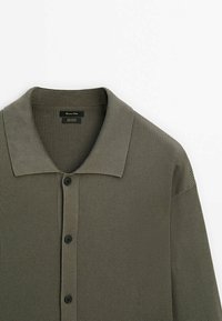 Olive green ribbed knit cardigan featuring a flat collar, buttoned front, and textured fabric. Labels indicate cotton material.