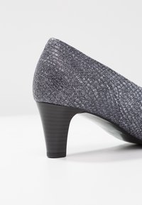 Šedá texturovaná lodička s vzorovaným vrchním materiálem a černým žeberkovým podpatkem, s lesklým interiérem, který se odráží.