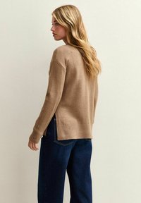 Brun stickad tröja med avslappnad passform, sidslitsar och ribbad mudd, kombinerad med mörkblå vida jeans. Slät textur, avslappnad stil.