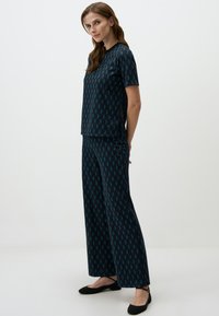 Donkerblauw pyjama set met geometrische turquoise patronen; T-shirt met korte mouwen, wijde broek en casual zwarte instappers. Gladde stof textuur.