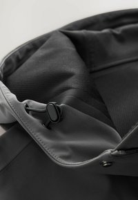 Gray multifunctional bag with a smooth exterior, drawstring closure, and textured black interior lining; includes a small fastener.