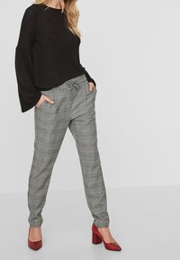 Black long-sleeve top, check patterned gray trousers with drawstring; red high-heeled shoes with textured finish. Simple background.