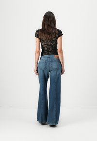 Haut en dentelle noire à manches courtes associé à un jean bleu taille haute à jambes larges, doté d'un design classique à cinq poches et d'une étiquette en cuir marron à l'arrière.