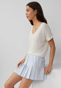 Haut blanc à manches courtes et en V associé à une mini-jupe plissée bleu clair. La jupe présente des rayures verticales et une texture lisse.