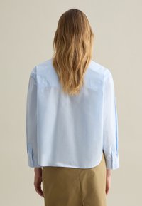 Camisa de manga larga de color azul claro con un corte relajado, puños con botones y dobladillo redondeado, hecha de un tejido suave y ligero.