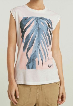 Sleeveless white top with a large blue and black abstract leaf print over a pink background worn with beige pants.