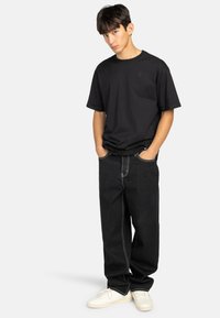 Zwarte katoenen t-shirt met een ronde hals en een klein ingebosseld logo, gecombineerd met loszittende zwarte denim jeans met contrasterende witte stiksels.