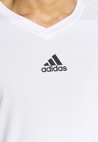 Witte Adidas v-hals T-shirt van gestructureerde stof, met een zwart trefoil-logo gecentreerd op de borst.