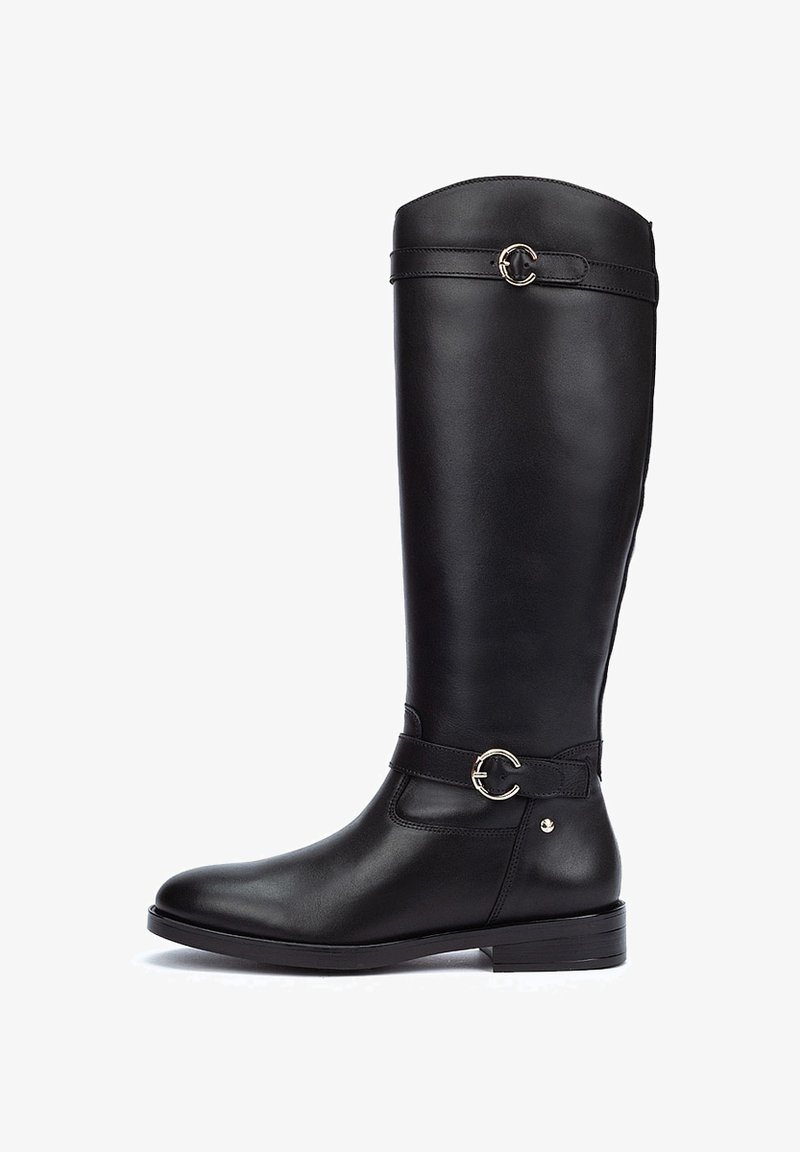 Botte en cuir noir montante, avec une texture lisse, accent de boucle circulaire sur la sangle et un petit talon empilé. Détail de couture latérale visible.