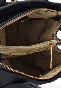 Interno di una borsa nera che mostra una foderatura in tessuto beige con script neri, una tasca con zip beige e un tirazip dorato.