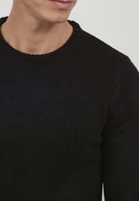 Kötött fekete kereknyakú pulóver, textúrált anyaggal és bordás nyakkal. Szoros illeszkedésű fazon, hosszú ujjakkal.