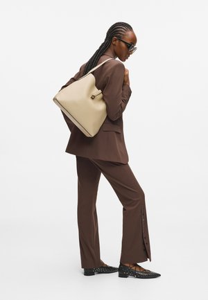 Brąsurowany garnitur z beżową torebką o wyraźnej strukturze. Teksturowane czarne baletki z ćwiekami oraz eleganckie okulary przeciwsłoneczne dopełniają całość.