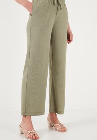 Pantalons à jambes larges vert olive avec une finition texturée, dotés d'une taille élastique à cordon de serrage ; portés avec des sandales à talons à brides beige clair.