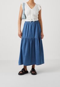 Vit spetsblus med volangärmar och V-ringning, kombinerad med en blå denimmaxikjol. Svarta sandaler fulländar looken.