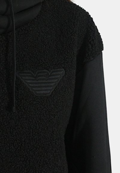 Pullover in fleece nero con superficie testurizzata, caratterizzato da un sottile patch del logo nero sul petto e un colletto alto per un maggiore comfort.