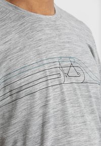 Ljusgrå melange T-shirt i mjukt tyg med blå och svarta linjeteckningar av en cykel och vågiga mönster över framsidan.