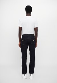 Σκούρο τζιν παντελόνι με ίσιες γραμμές, πέντε τσέπες και χρυσά αξεσουάρ, συνδυασμένο με ένα απλό λευκό μπλουζάκι και λευκά αθλητικά παπούτσια.