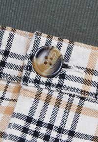 Gros plan d’un tissu à carreaux beige, noir et blanc avec un bouton rond marbré cousu et un tissu côtelé vert au-dessus.