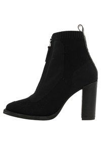 Bottine noire en tricot avec un talon carré, fermeture éclair sur le côté, motif texturé et patte de tirage à l'arrière.