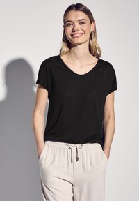 T-shirt nero con scollo a V realizzato in tessuto morbido, progettato con maniche corte. Abbinato a pantaloni beige chiaro con vita elastica e cordino.