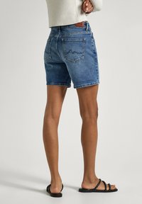 Shorts de mezclilla en azul claro con un ajuste relajado, diseño de cinco bolsillos y dobladillo enrollado. Combinados con sandalias negras de tiras.