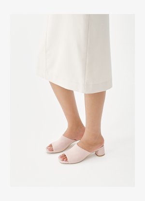 Πόδια με φόρεμα midi σε εκρού χρώμα και μπεζ ροζ ανοιχτά mules με χοντρό τακούνι σε λευκό φόντο.
