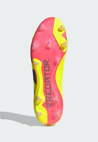 Semelle de crampons de football en rose vif, jaune et noir. Présente des crampons rectangulaires proéminents et un marquage "PREDATOR" en gris. Surface texturée.
