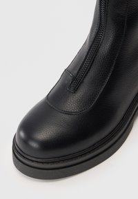 Zwarte leren enkelboot met ritssluiting, ronde neus, gestructureerde afwerking en een dikke rubberen zool voor extra duurzaamheid.