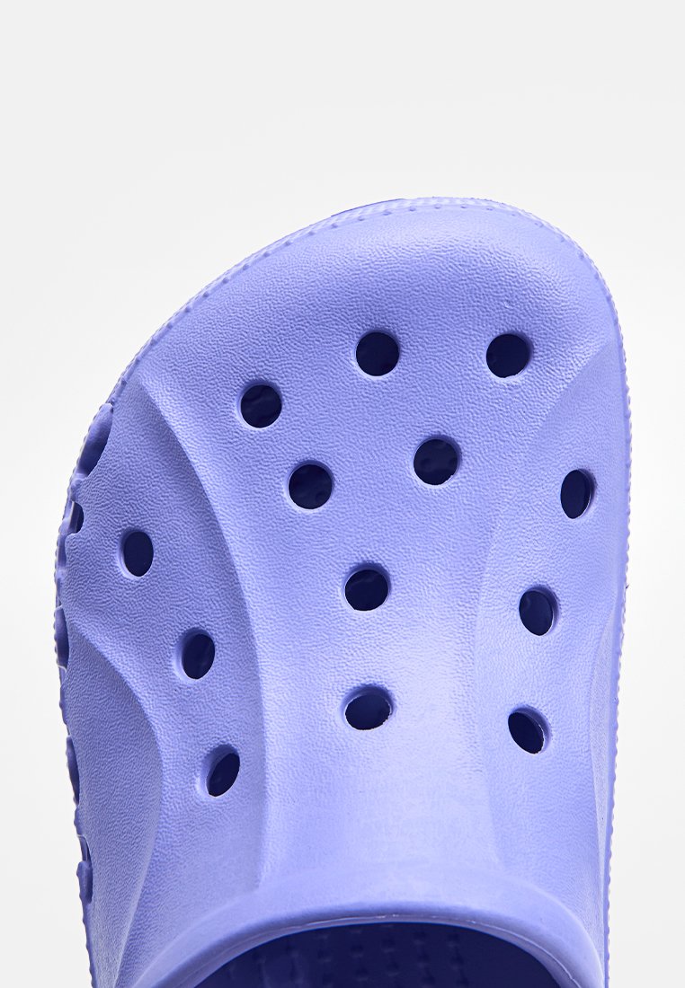 Zuecos morados hechos de un material similar al caucho que presentan múltiples agujeros de ventilación, una forma curvada y una superficie texturizada para mejorar el agarre.