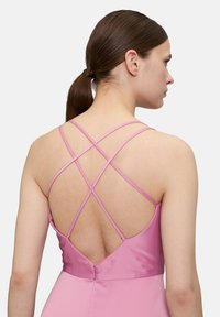 Różowa sukienka z krzyżującymi się ramiączkami z tyłu, dopasowaną górą i ukrytym zapięciem na zamek, wykonana z gładkiego, teksturowanego materiału.