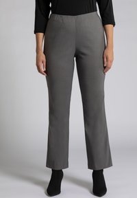 Grijze wijde broek met een elastische tailleband, gemaakt van een gladde stof. Draagt met zwarte enkellaarzen met hakken.