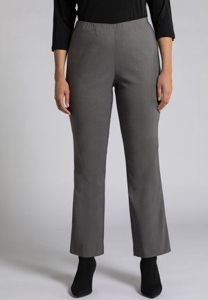 Grijze wijde broek met een elastische tailleband, gemaakt van een gladde stof. Draagt met zwarte enkellaarzen met hakken.