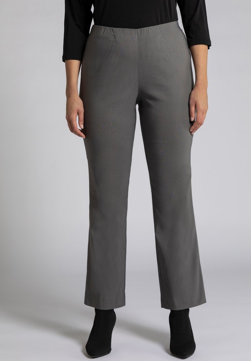 Grijze wijde broek met een elastische tailleband, gemaakt van een gladde stof. Draagt met zwarte enkellaarzen met hakken.